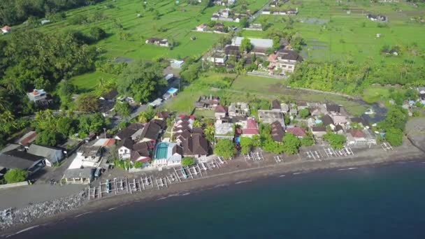 Latanie z laguny oceanicznej w kierunku pięknej, egzotycznej plaży z czarnym piaskiem. Ośrodek hotelowy z dużymi bungalowami nad morzem z basenem wśród palm. Bali, Indonezja. Koncepcja podróży, Nagrania lotnicze — Wideo stockowe