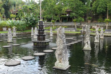 Water Palace Tirta Gangga on Bali island, Indonesia. Labyrinth of decorated stone steps on the water in an artificial lake with statues on a background clipart
