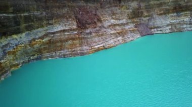 Turkuaz Kelimutu krater gölü güneşli bir günde renkli kayalık duvarlarla çevrilidir. Ende Flores Adası Endonezya 'nın güzel doğa manzarasını düşünün. 4K atışı. Hava görüntüsü çok renkli göller