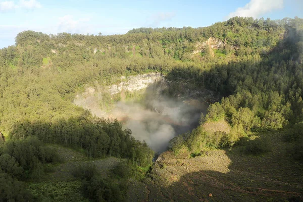 The dark blue lagoon waters of one of the three sacred lakesof Kelimutu, Indonesia. Trees surround the crater and misty clouds roll in over the top — Stock Photo, Image