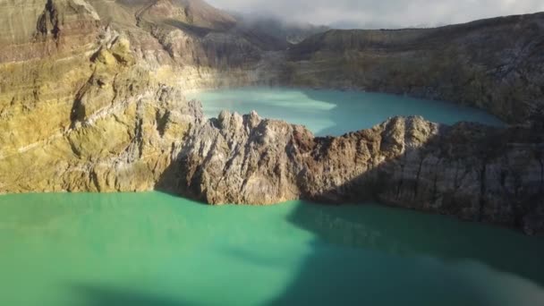Полет над озерами Вуланис на небольшой высоте. Крупный план скальной стены, разделяющей красочные озера. Келимуту трёхцветный вулканический кратер, покрытый туманом, имеет вид с воздуха. Флорес, Индонезия — стоковое видео