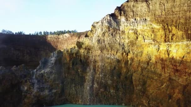 Vista de perto para paredes coloridas de crateras sobre lagos vulcânicos. O drone volta atrás acima da superfície do lago colorido. os raios de sóis iluminam as rochas circundantes — Vídeo de Stock