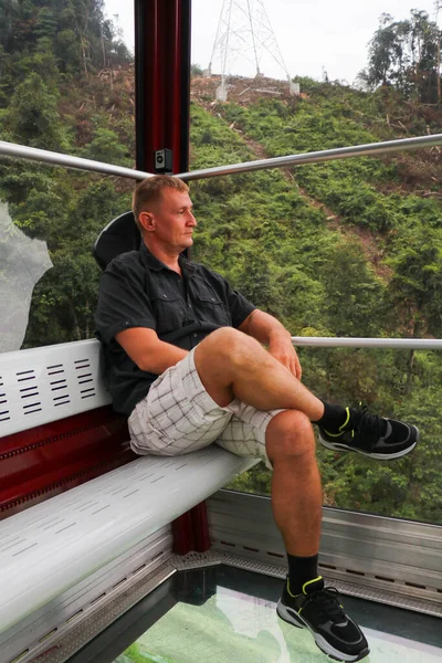 Terra vista através do chão de vidro de uma cabana de cristal. Homem em cabine de teleférico com piso de vidro. Passeios turísticos no teleférico. Genting Highland, Malásia — Fotografia de Stock