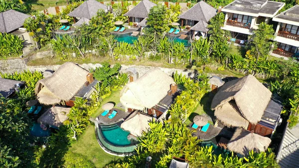 Tropikal ormanlarda ve palmiye ağaçlarında saman çatı villaları ve havuzları olan lüks otelin havadan görünüşü. Lüks villa, ormandaki pavyon, Ubud, Bali — Stok fotoğraf