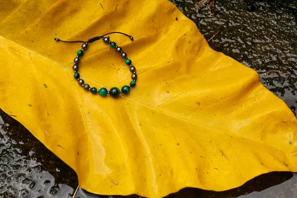 Ein Armband runde Perlen auf gelb grünen Blättern mit Steinhintergrund — Stockfoto