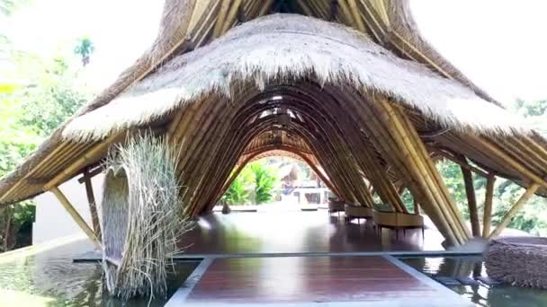 Voar através de um barracão de bambu com um telhado de cana em Ubud, Bali. Vista aérea o telhado de uma casa grande com palha seca e feno. teto de bambu com luz do sol — Vídeo de Stock