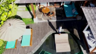 Bali 'de tatilde lüks bir mülkte yüzme havuzunun yanındaki genç adam. Hava görüntüsü 4K