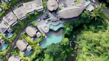 Tropikal ormanlarda ve palmiye ağaçlarında saman çatı villaları ve havuzları olan lüks otelin havadan görünüşü. Lüks villa, ormandaki pavyon, Ubud, Bali