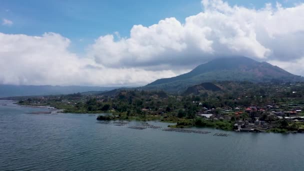 Voo de baixo ângulo sobre o Lago Batur. Gaiolas de bambu na superfície da água. Viveiros de pescadores locais. No fundo o vulcão Batur — Vídeo de Stock