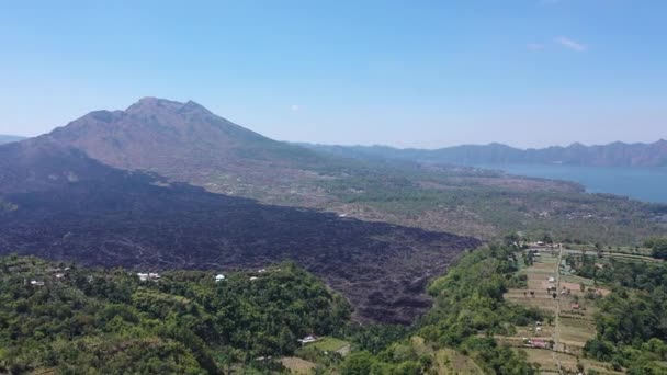 Antenn: Flyger ovanför grov steniga svart lava terräng och grå ashy vulkaniska jorden på toot av Mount Batur mot toppen av bergskedjan. Dramatiska landskap Kintamani vulkan kratern, Bali — Stockvideo