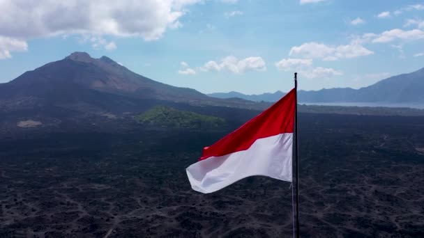 Indonezyjska flaga wieje na wietrze wulkanu Batur. Czerwono-biała indonezyjska flaga trzepocze na wietrze odizolowanym na tle błękitnego nieba — Wideo stockowe