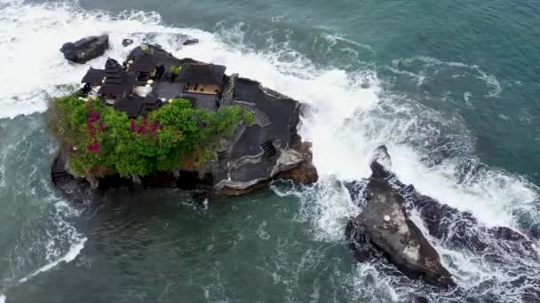 Silne fale morskie uderzające w skalisty klif ze świątynią Tanah Lot na Bali w Indonezji. Zdjęcia lotnicze krążące wokół słynnej miejscowości turystycznej na morzu — Wideo stockowe