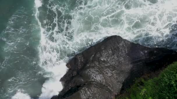 Top uitzicht vanuit de lucht van vliegende drone zoomen omhoog van verbazingwekkende zee landschap met turquoise water grote schuimende golven en zwarte rotsen. Zwart zandstrand, Bali Indonesië — Stockvideo