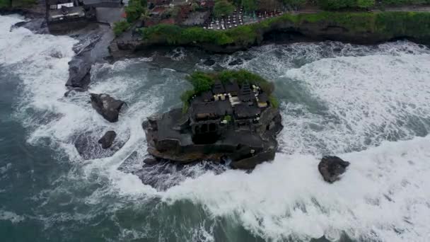 Templo vacío de Tanah Lot en el acantilado rocoso oscuro en el mar durante el tiempo de bloqueo covid. Marea alta y clima peligroso. Tiro aéreo giratorio de olas estrellándose en tierra el templo hindú en Bali, Indonesia — Vídeos de Stock