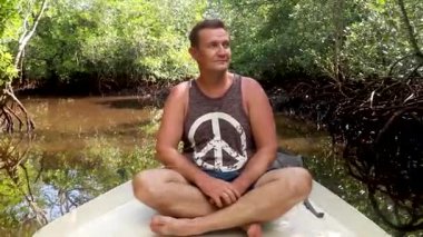 Orta yaşlı bir adam gölde kayıkla kayıkla geziyor mangrov kökleri ve ağaçlarının arasında. Kafkasyalı turist bir mangrov ormanında tekneye biniyor.