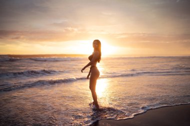 Gün batımında deniz plajda üstsüz ince gövdeli seksi kadın