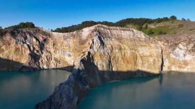 Close up view of features Kelimutu striking cliffs bathed in sunlight, dividing the peaceful volcanic lakes below.
