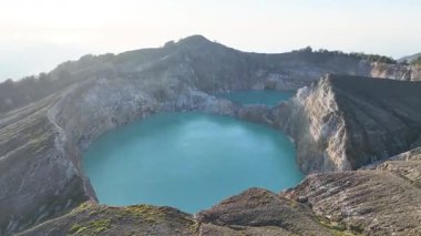 Fiery sunrise silhouettes Kelimutu crater lakes, with radiant turquoise waters shining beneath golden mountain peaks along the enigmatic Flores skyline.