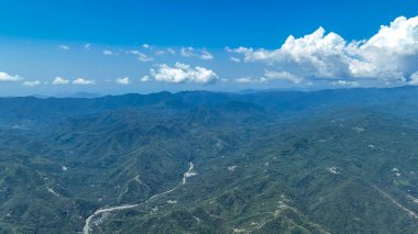 Towering clouds drift above endless green hills and valleys as winding rivers carve through the landscape, painting a picture of Flores mystical highlands.