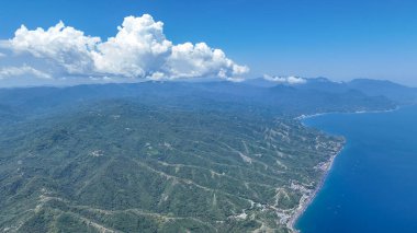 Dramatic clouds float above rolling green hills, where a winding coastline meets the vivid blue sea in a stunning aerial view of Flores.