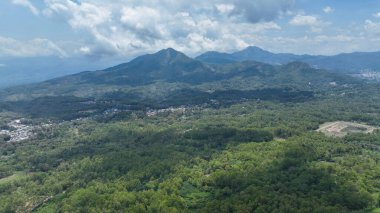 Wolobobo Dağı 'nın panoramik manzarası. Engin mavi gökyüzünün altındaki verimli ormanlara, yuvarlanan tepelere ve uzak tepelere hükmediyor..