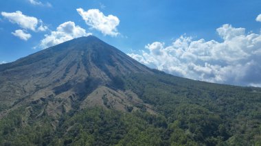 Görkemli Inerie Dağı ufka hükmediyor. Heykeltraş edilmiş lav sırtları yoğun yeşil yamaçlara ve dalgalı bulutlara akıyor..