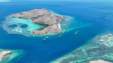 Beyaz şeker bulutları altında, Komodo dağınık adalar ve resif platformları yavaş hareket eden canlı canlı gemilerle çaprazlanmış canlı bir deniz manzarası oluşturur..