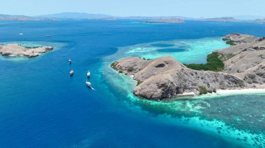 Gemideki canlılar Komodo kristal kanalında kurak tepeler ve parlayan resiflerin yanında geziyorlar. Derin mavi, neon sığ sularla birleşir, uzak adaların çerçeve ufkuyla. Kaşifler için nihai deniz manzarası.