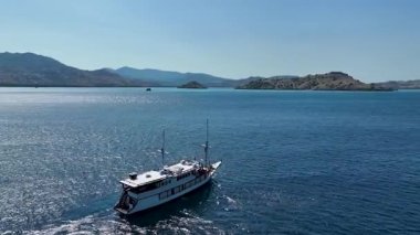 Geleneksel bir Endonezya ahşap botu fenisi güneşli bir gökyüzünün altında sakin, derin mavi deniz sularında yüzer..