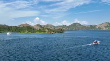 Zarif beyaz pinisi, uzak ufukta görkemli bir şekilde yükselen yeşil volkanik tepelerle derin mavi sularda tek başına süzülüyor..