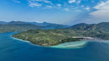 Turkuaz lagünün derin okyanusla ve tropik görkemli yeşil dağlarla tezat oluşturduğu kıyı şeridindeki köy levrekleri.