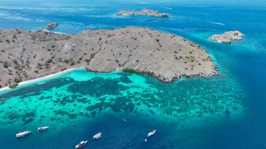 Komodo 'nun çorak tepelerinin eteklerindeki parlayan turkuaz resifler üzerinde kayıklar sürükleniyor. Orada el değmemiş mercan bahçeleri derin mavi kanallar ve sonsuz ada ufkuyla kesişiyor..