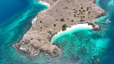 Serene Pantai Merah, Komodo Adası 'nda, ünlü pembe sahil ve ahşap iskelenin yanındaki zümrüt ambarları süsleyen tekneler..