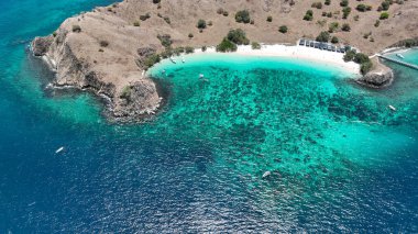 Canlı resifler ve demirlemiş filo çerçeveleri Komodo Adası 'ndaki Pantai Merah beyaz pembe plajı, kurak uçurumların ortasındaki bir dalgıç cenneti..
