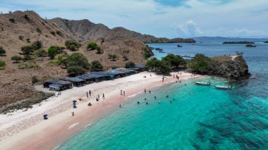 Pembe plaj boyunca pembe kum kıvrımlarından oluşan yumuşak bir kurdele, renkli havlular ve zümrüt suyla kaplı yüzücüleri resife davet ediyor..