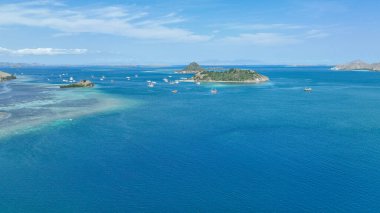Resif rafları ve adacıklar, derin mavi denizde beyaz taç yaprakları gibi dağılmış klasik tekneleri olan bir Komodo kanalı çerçeveler..