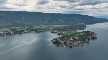 Tuk Tuk ormanı burunları kaplayarak Toba Gölü 'ne uzanır. Batak çatıları ve parlak havuzları Samosir Adası' nın karanlık volkanik kayalıklarına karşı parlar..