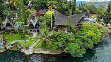 Samosir Adası kıyısında yükselen çatıları olan ikonik Batak evleri, Sumatra, Toba Gölü 'ne dökülen tropikal bahçeler..