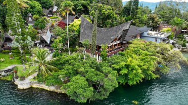 Samosir, Sumatra 'da bulunan geleneksel Batak hangarları, derin mavi suların üzerinde palmiyeler ve yemyeşil sularla kaplı..