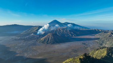 Sabah ışığı, ufuktaki Semeru 'nun yükselen siluetiyle desteklenen kraterinden yükselen buharla Bromo Dağı' nın sırtlarını fırçalıyor..