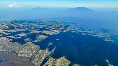 Güneş, uzak Semeru 'yu ve engin kalderayı katmanlı mavi gölgelerle örten sis gibi altın tepeleri kavurur..