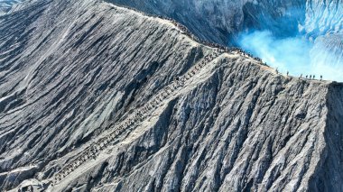 İz, Bromo 'nun dumanı tüten mavi kalbine kadar uzanır. Dalgalı kül yamaçları ve uzak sisli tepelerle çevrilidir..