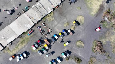 Gökkuşağı renkli jip ve çadırlardan oluşan kaotik bir filo Kum Denizi 'ne yayılarak, bitmek bilmeyen volkanik griliğin ortasında tapınağı çerçeveliyor..