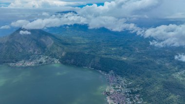 Batur Caldera zümrüt gölü dramatik uçurumlar boyunca zarifçe kıvrılır, yemyeşil ormanlar ve sakin hava uyumu içinde uzak tepeler arasında göl kenarı köylerini kucaklar..