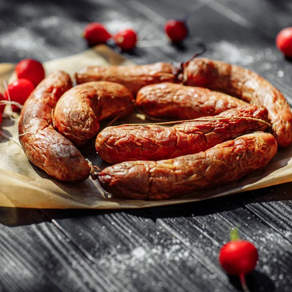 Smoked sausage on a wooden rustic table with addition of fresh aromatic herbs and spices, natural product from organic farm, produced by traditional methods. High quality photo
