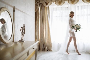 Penceresinde düğün buketi olan güzel bir gelinin portresi. Kıvırcık saçlı ve moda makyajlı sarışın kız. Yüksek kalite fotoğraf