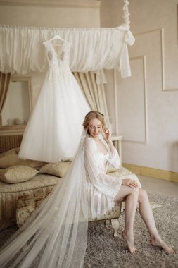 Düğün için. Evdeki gibi beyaz stüdyo içinde, güzel elbiseli gelin kanepede oturuyor. Modaya uygun bir düğün fotoğrafı. Yüksek kalite fotoğraf