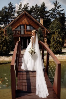 Güzel elbiseli güzel bir gelin, nehrin arka planında, ahşap bir köprüde duruyor. Saçında çiçekler var. Yüksek kalite fotoğraf