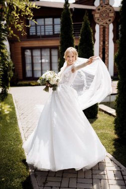 Yeşil bir bahçede duran, elinde çiçek ve yeşillik buketi olan bir gelinlik içinde gelin. Yüksek kalite fotoğraf