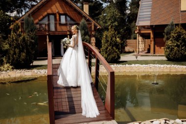 Güzel elbiseli güzel bir gelin, nehrin arka planında, ahşap bir köprüde duruyor. Saçında çiçekler var. Yüksek kalite fotoğraf